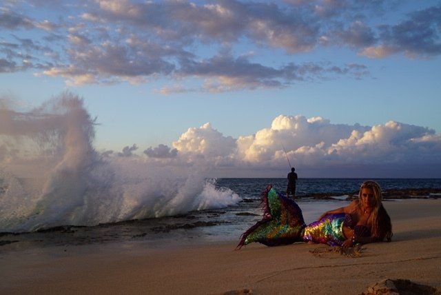 A mermaid is laying on the beach next to a wave.
