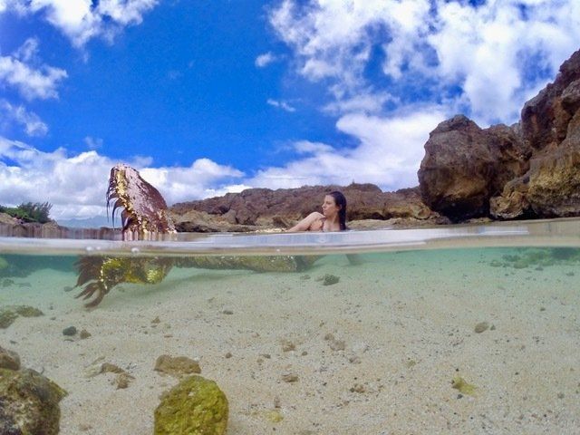 A woman is swimming in the ocean with a mermaid tail.