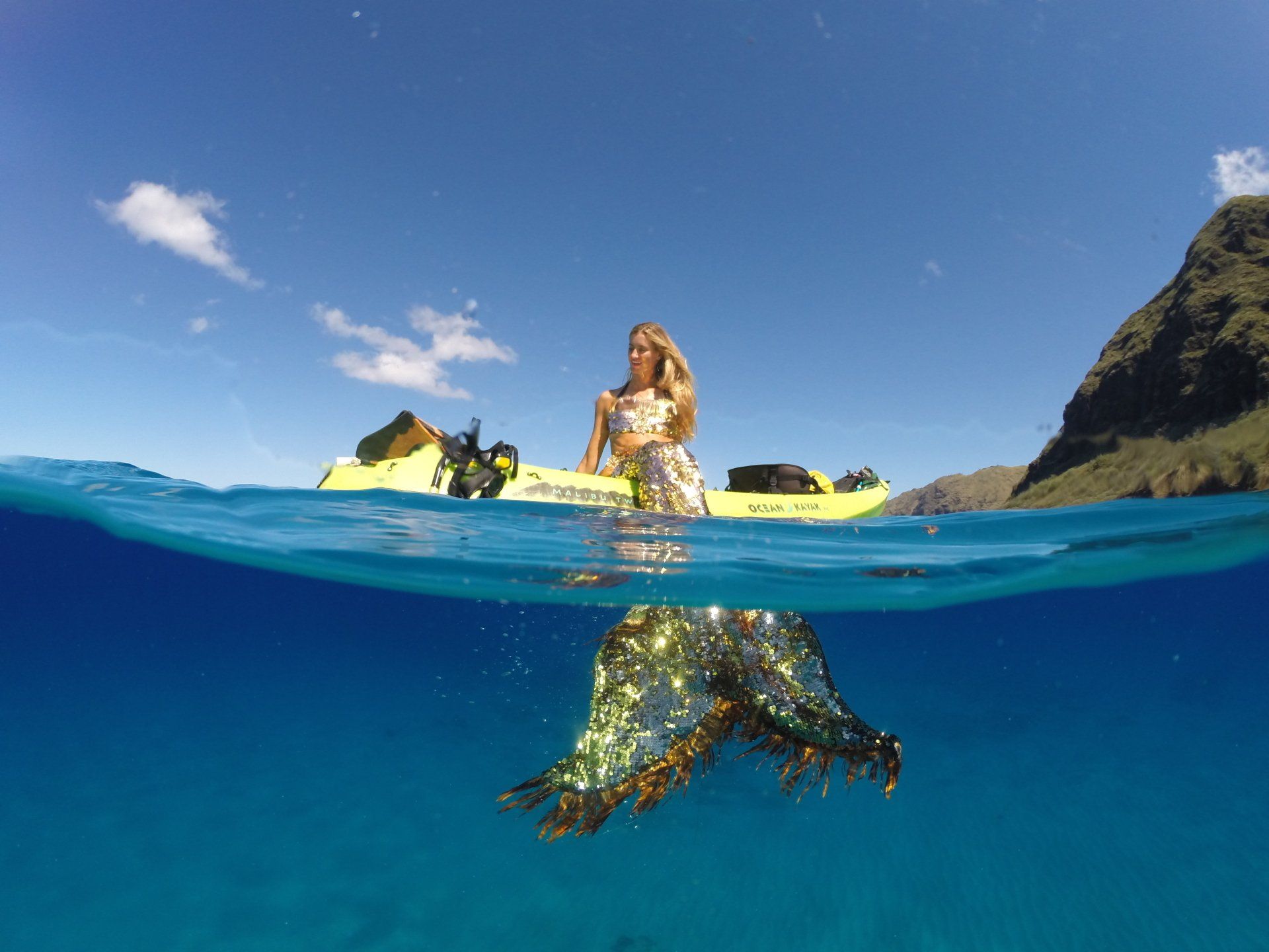 A woman in a mermaid costume is sitting on a kayak in the ocean.