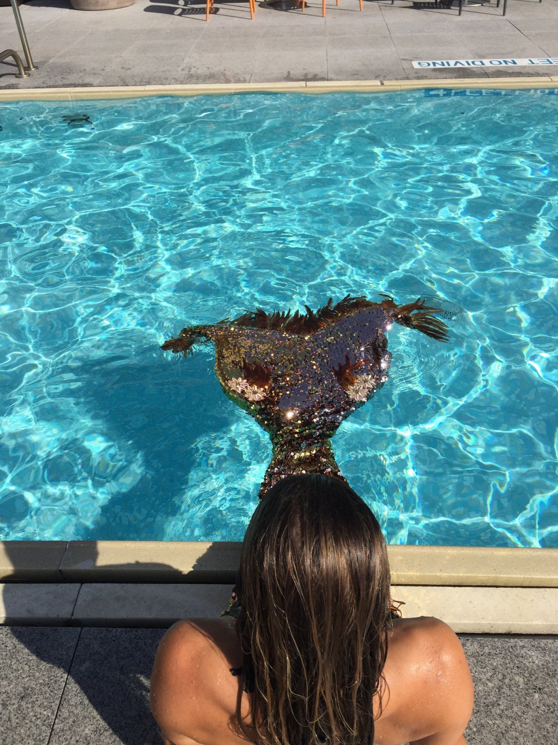 A woman in a mermaid costume is sitting on the edge of a swimming pool.