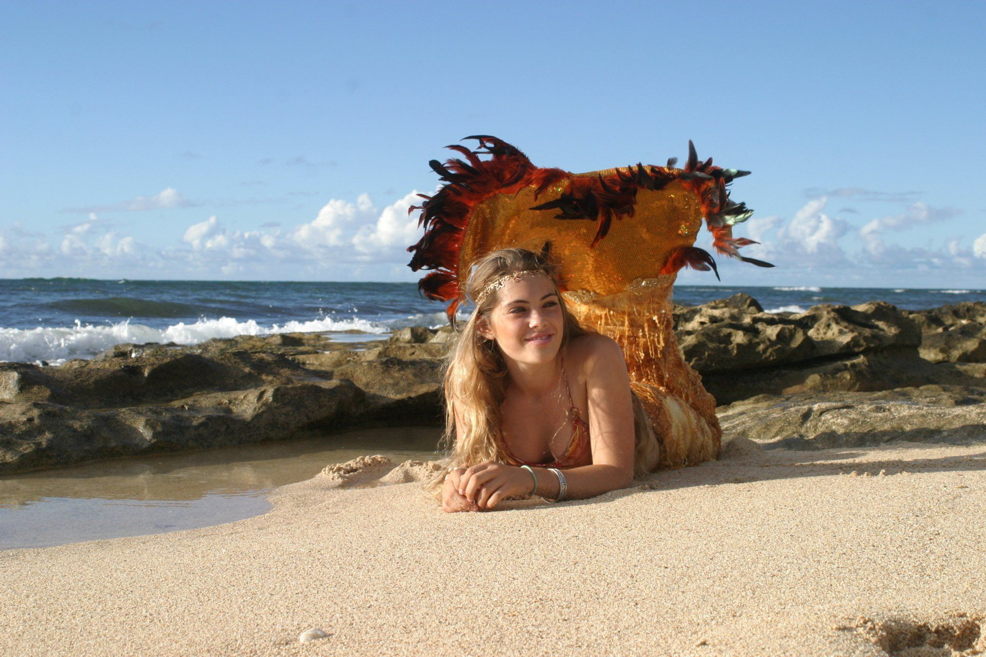 A woman in a mermaid costume is laying on the beach