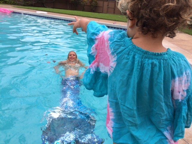 A little girl is pointing at a mermaid in a pool.