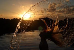 A woman is throwing her hair into the water at sunset.