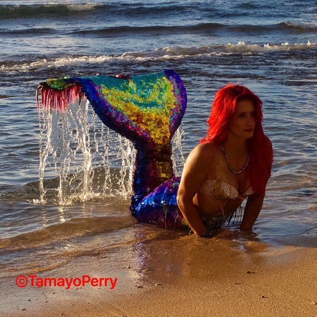 A woman in a mermaid costume is laying on the beach