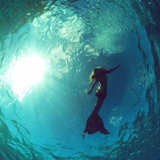 A mermaid is swimming in the ocean with the sun shining through the water.