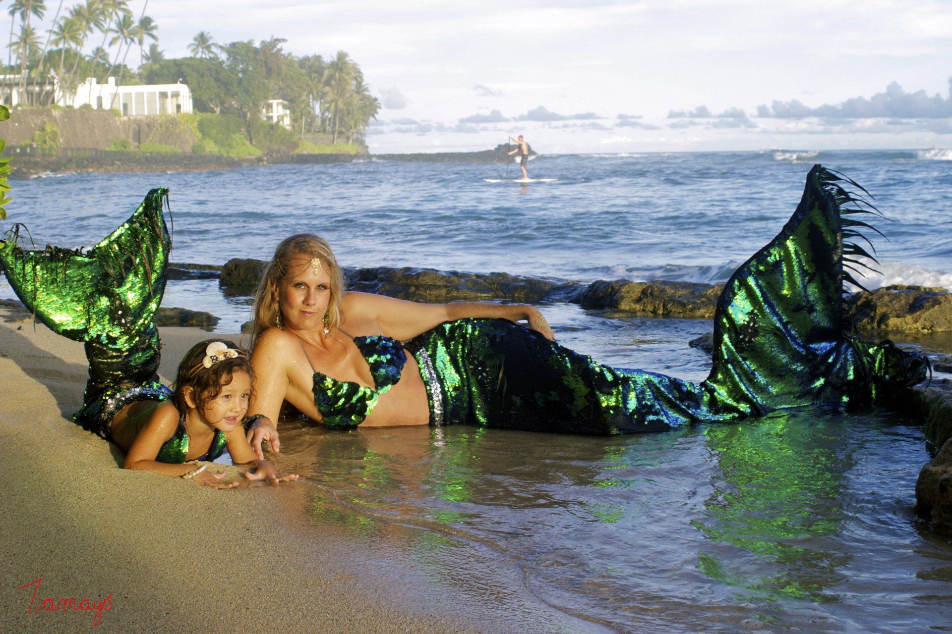 A woman and a little girl are dressed as mermaids on the beach
