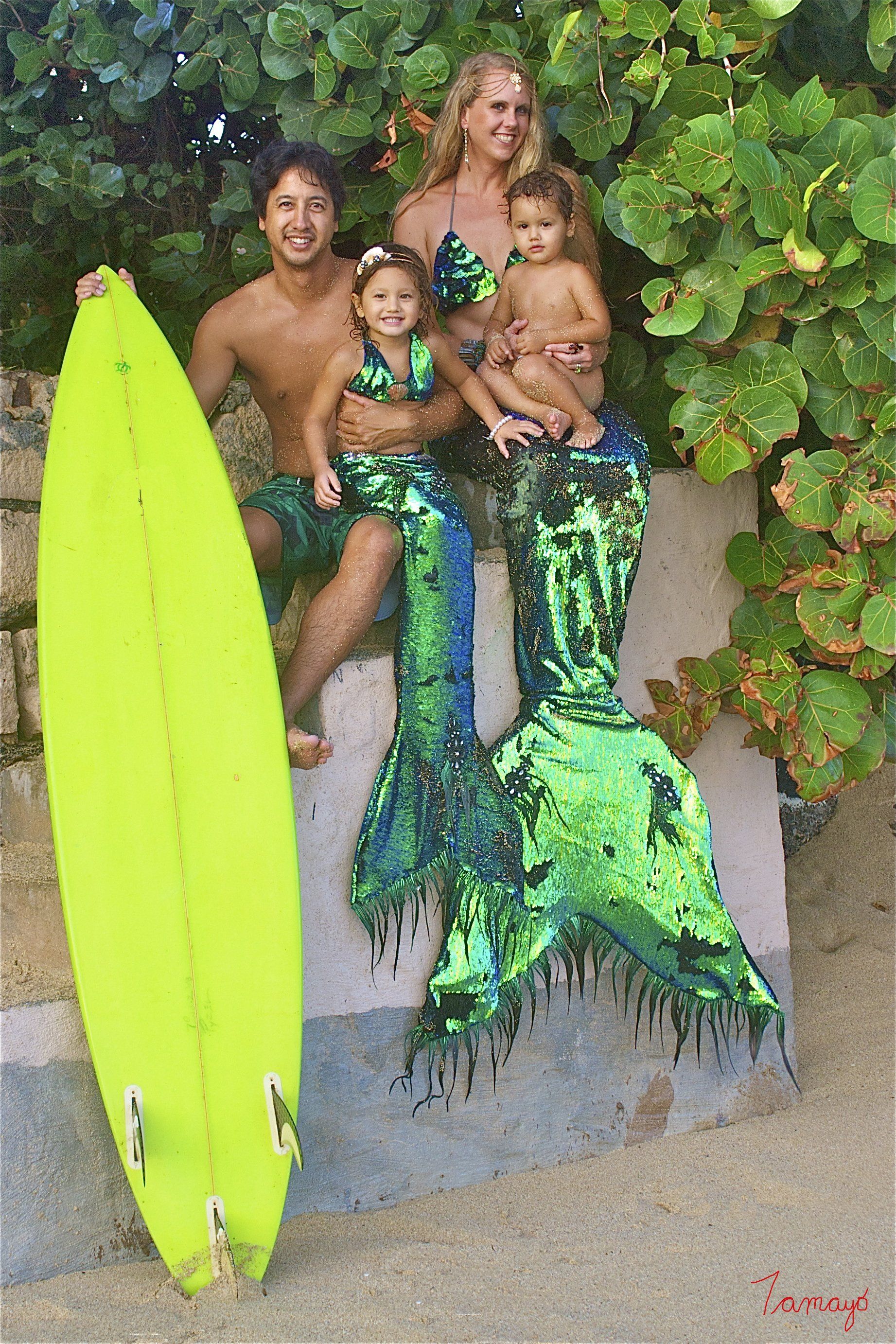A family is posing for a picture with a mermaid tail and a surfboard.