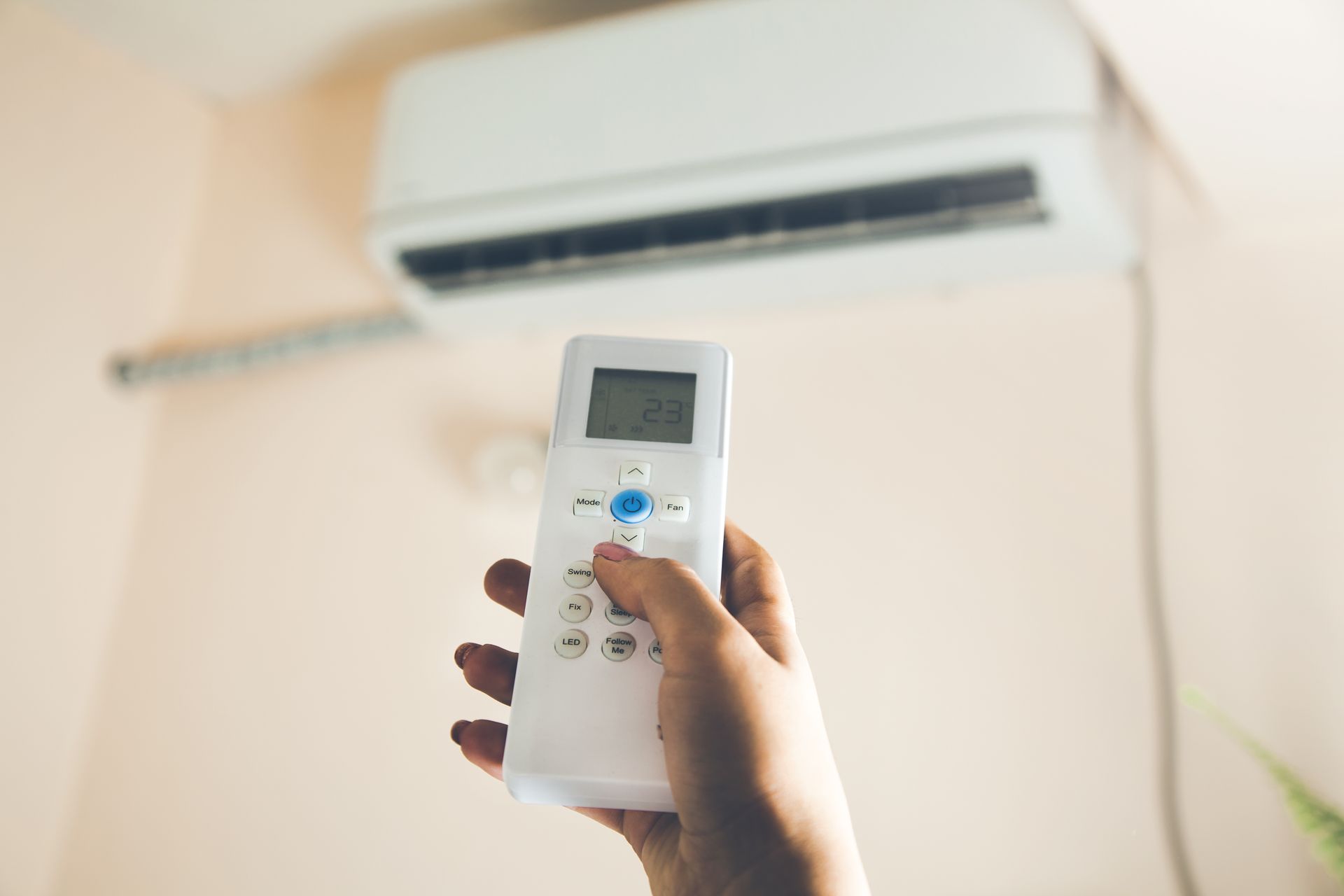 A hand holds a white air conditioner remote pointed at a wall-mounted unit.