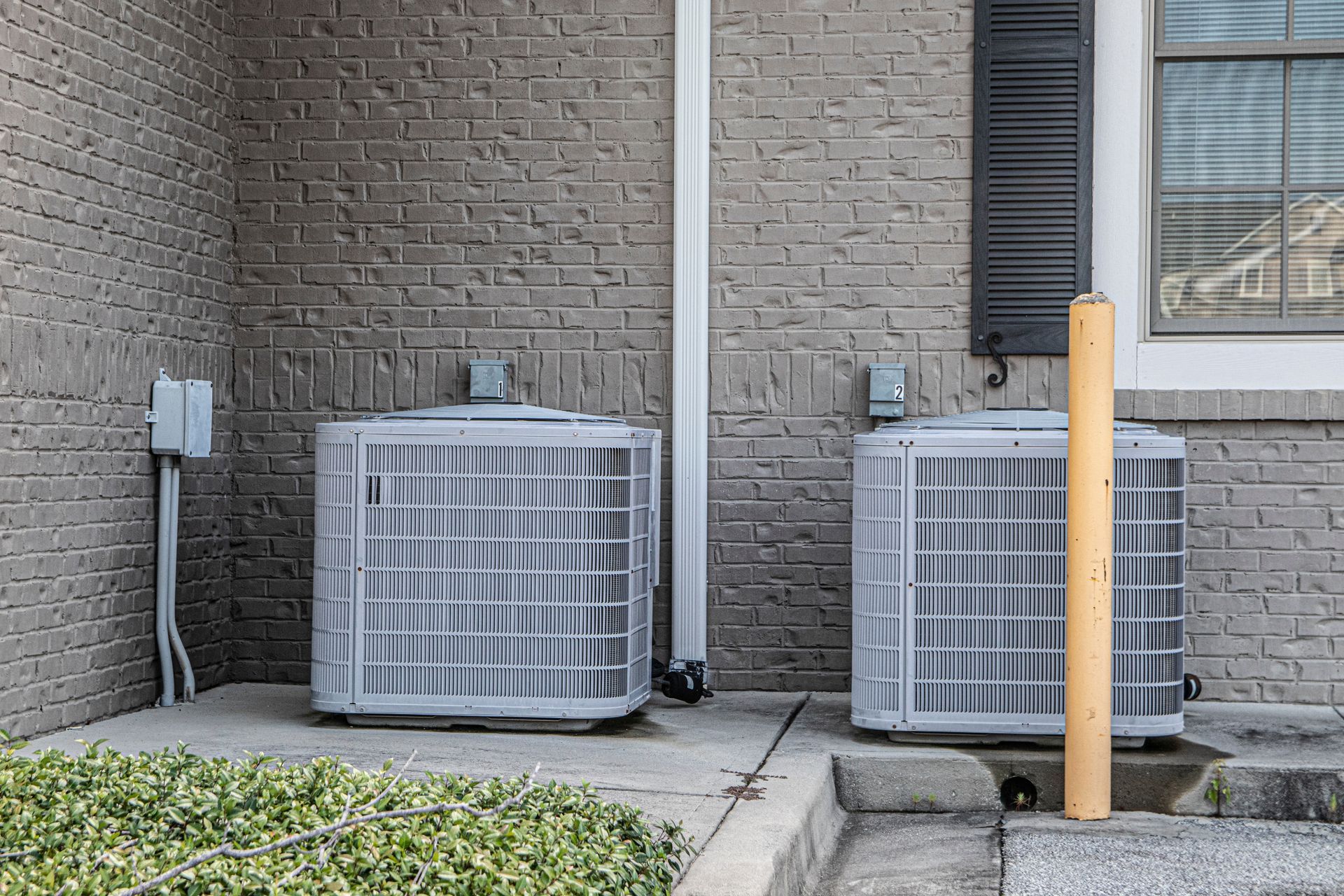 A technician in a high-visibility vest uses a manifold gauge set to service an outdoor air conditioning unit.