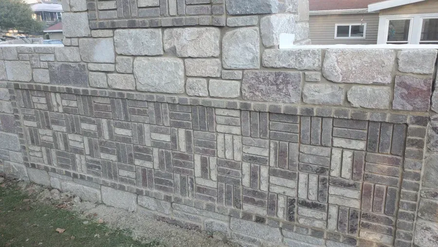 A stone wall with a brick border and a house in the background.