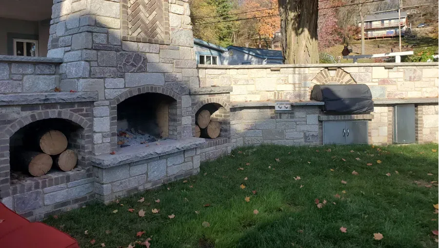 A brick fireplace with logs in it in a backyard.