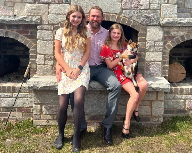 A man and two girls are sitting on a stone bench with a dog.