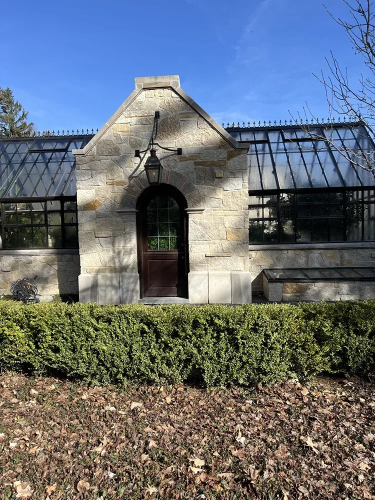 A greenhouse is surrounded by bushes and leaves on a sunny day.