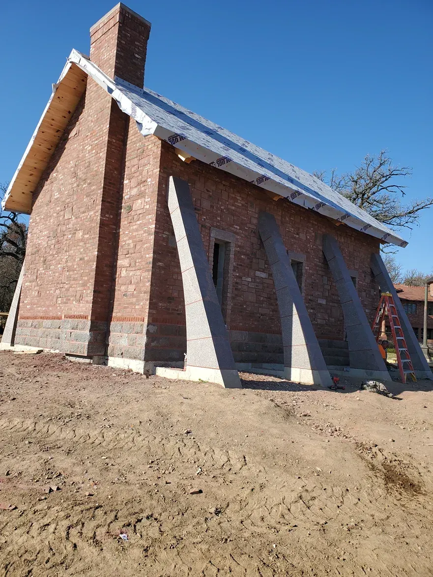A brick building with a chimney is being built in the middle of a dirt field.