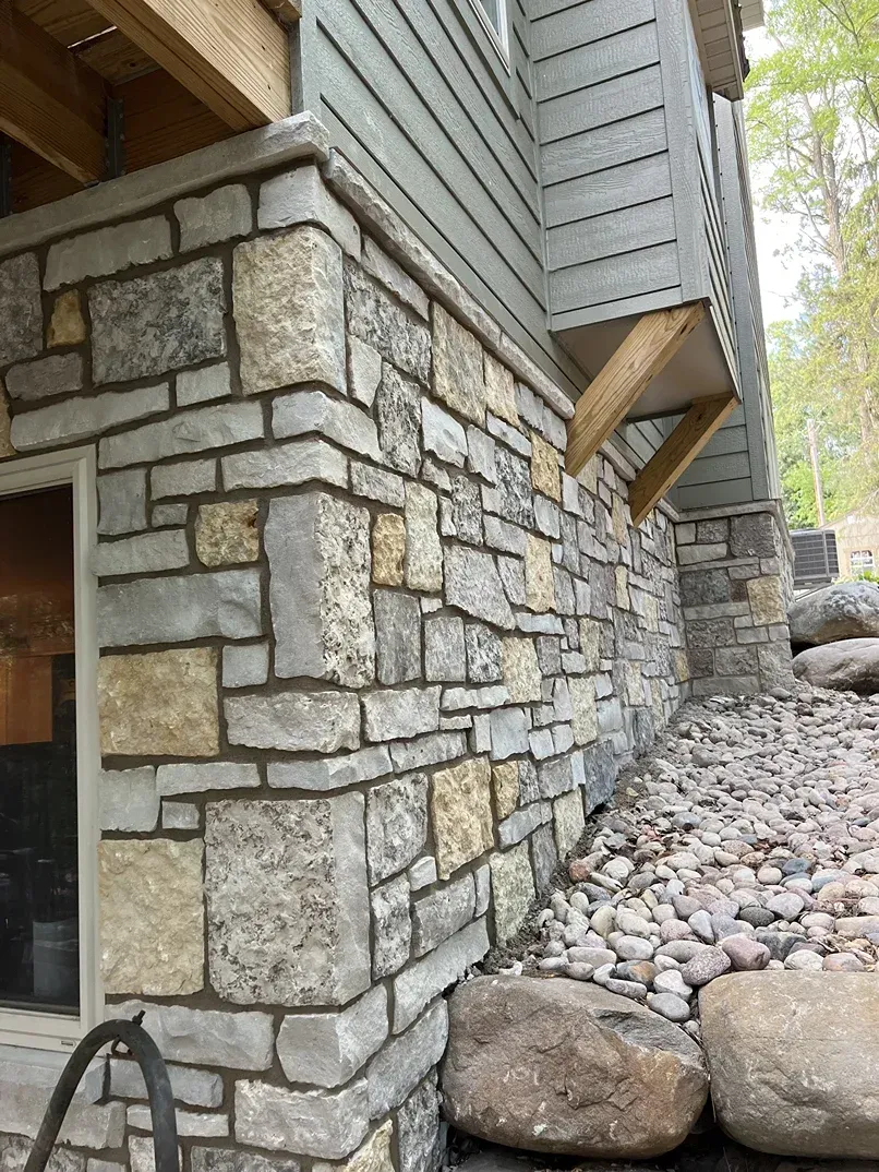 The side of a house with a stone wall and rocks.