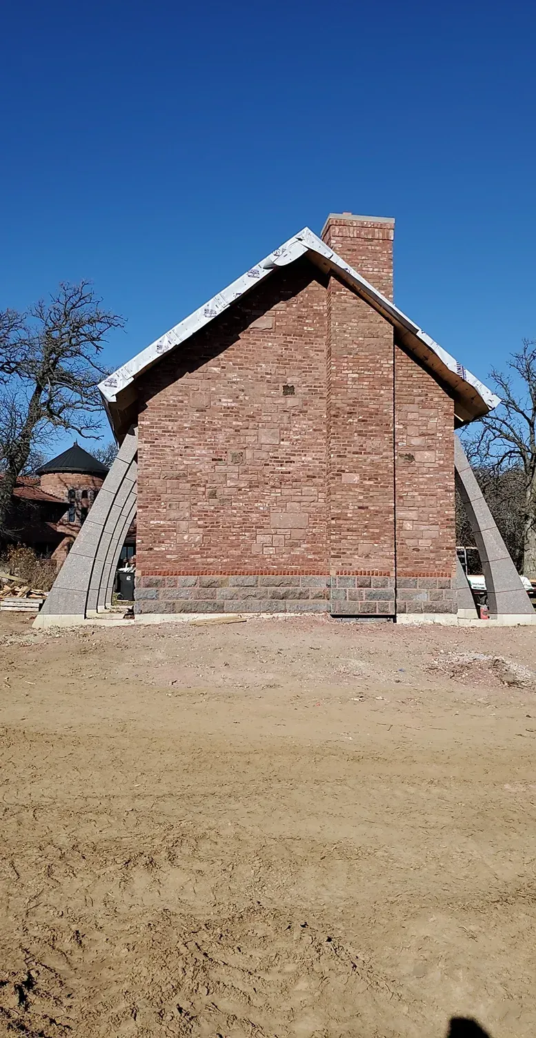 A brick house with a chimney is being built in a dirt field.