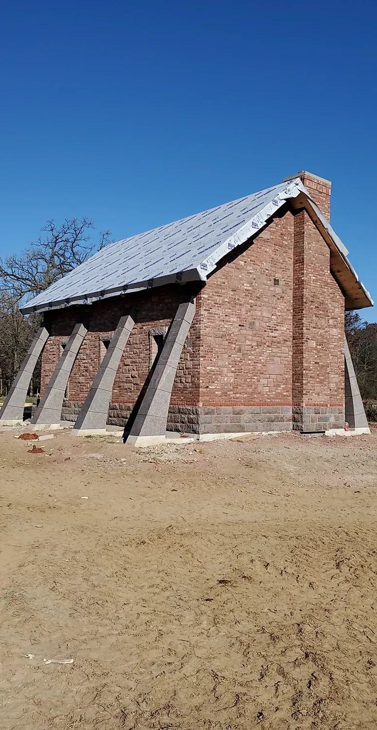 A small brick building with a metal roof is sitting in the middle of a dirt field.