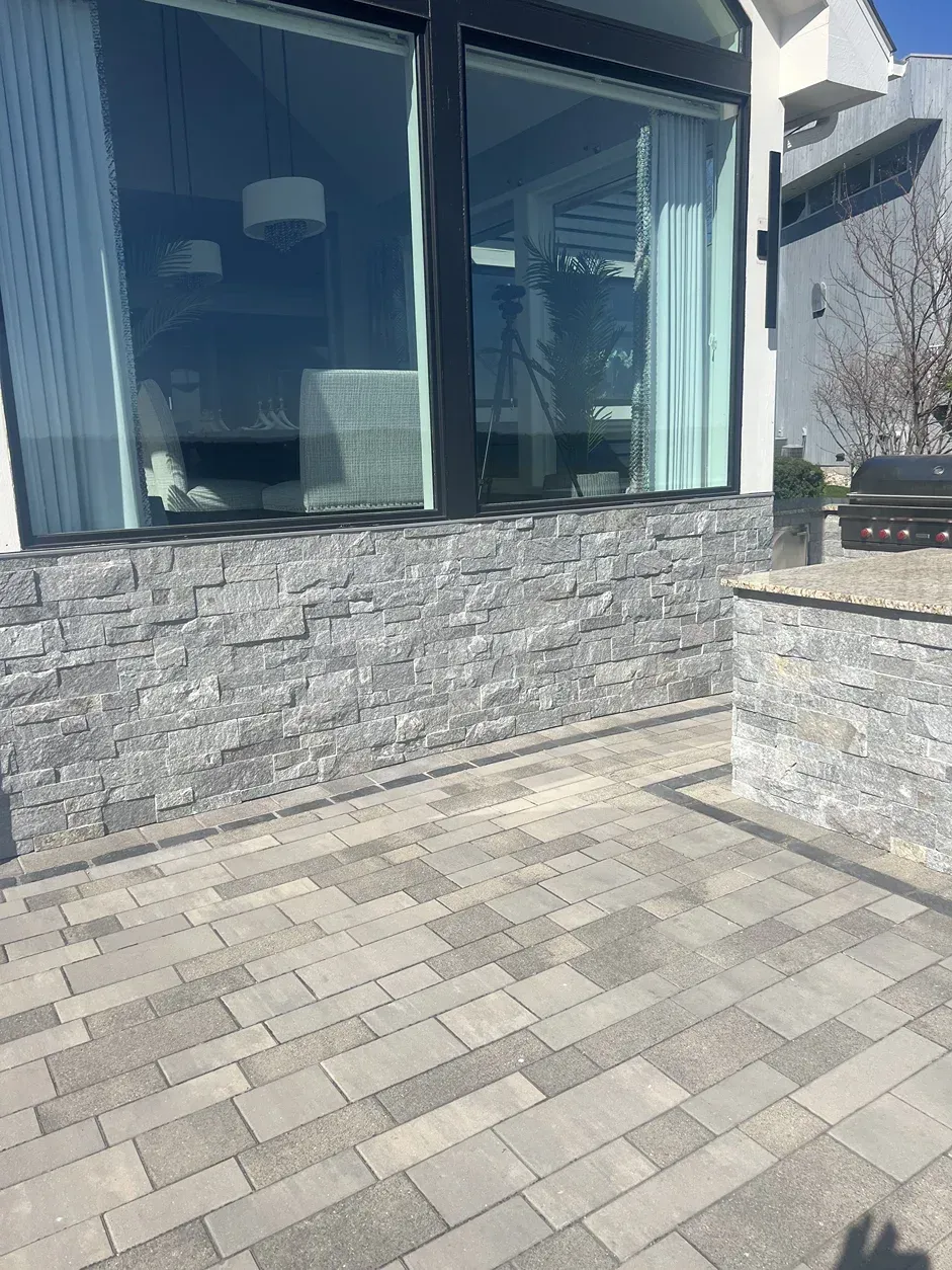 A brick wall with a large window and a patio in front of it.