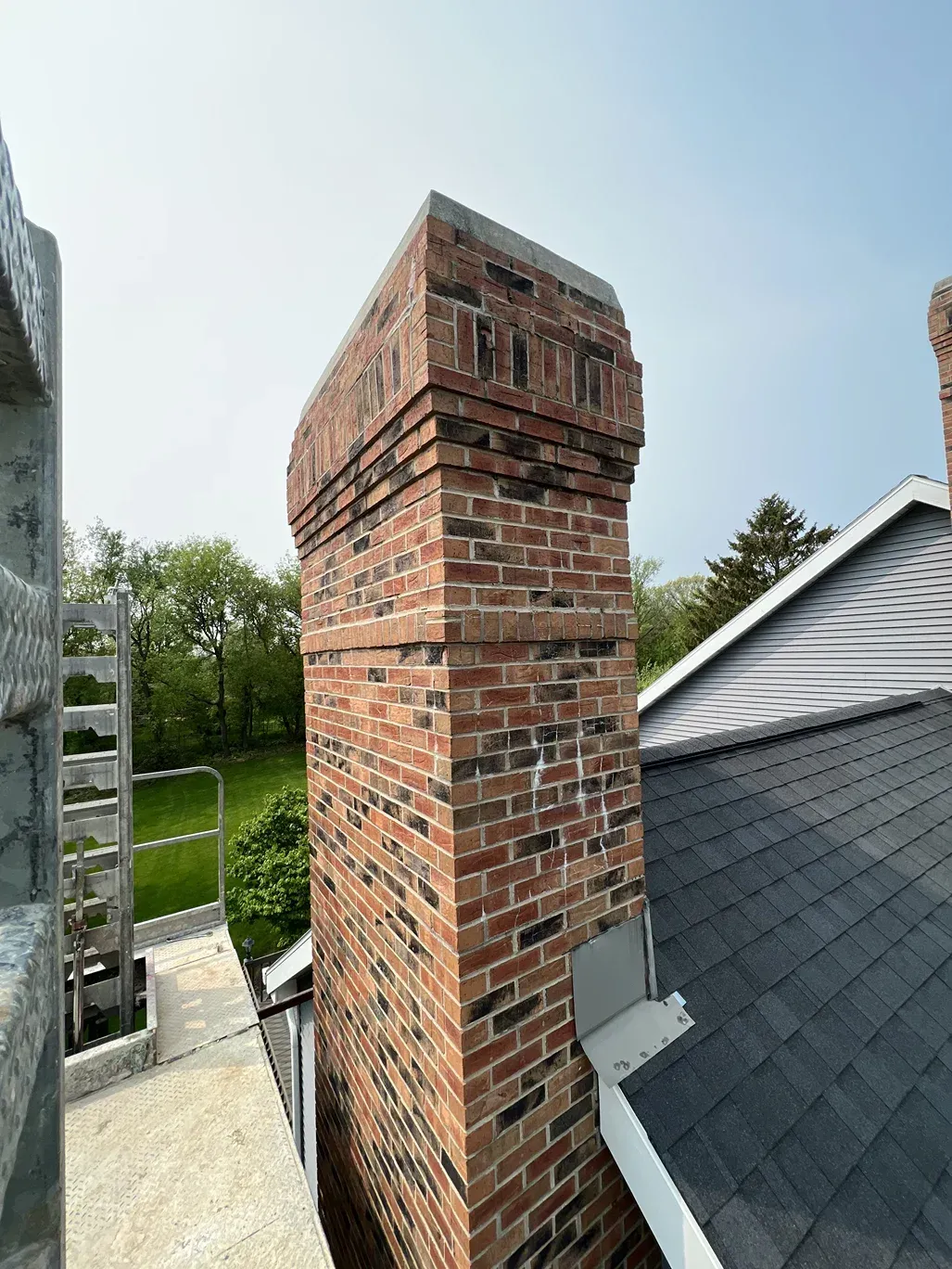 A brick chimney is sitting on top of a roof next to a house.