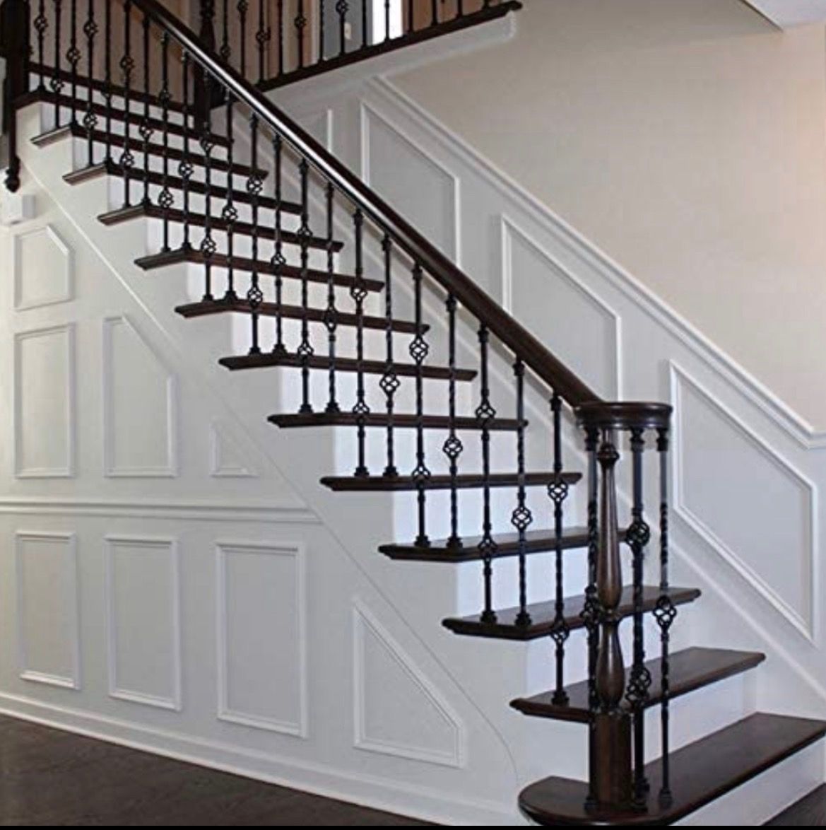 Staircase with dark wood treads and banister, ornate black metal balusters, and white paneled walls.