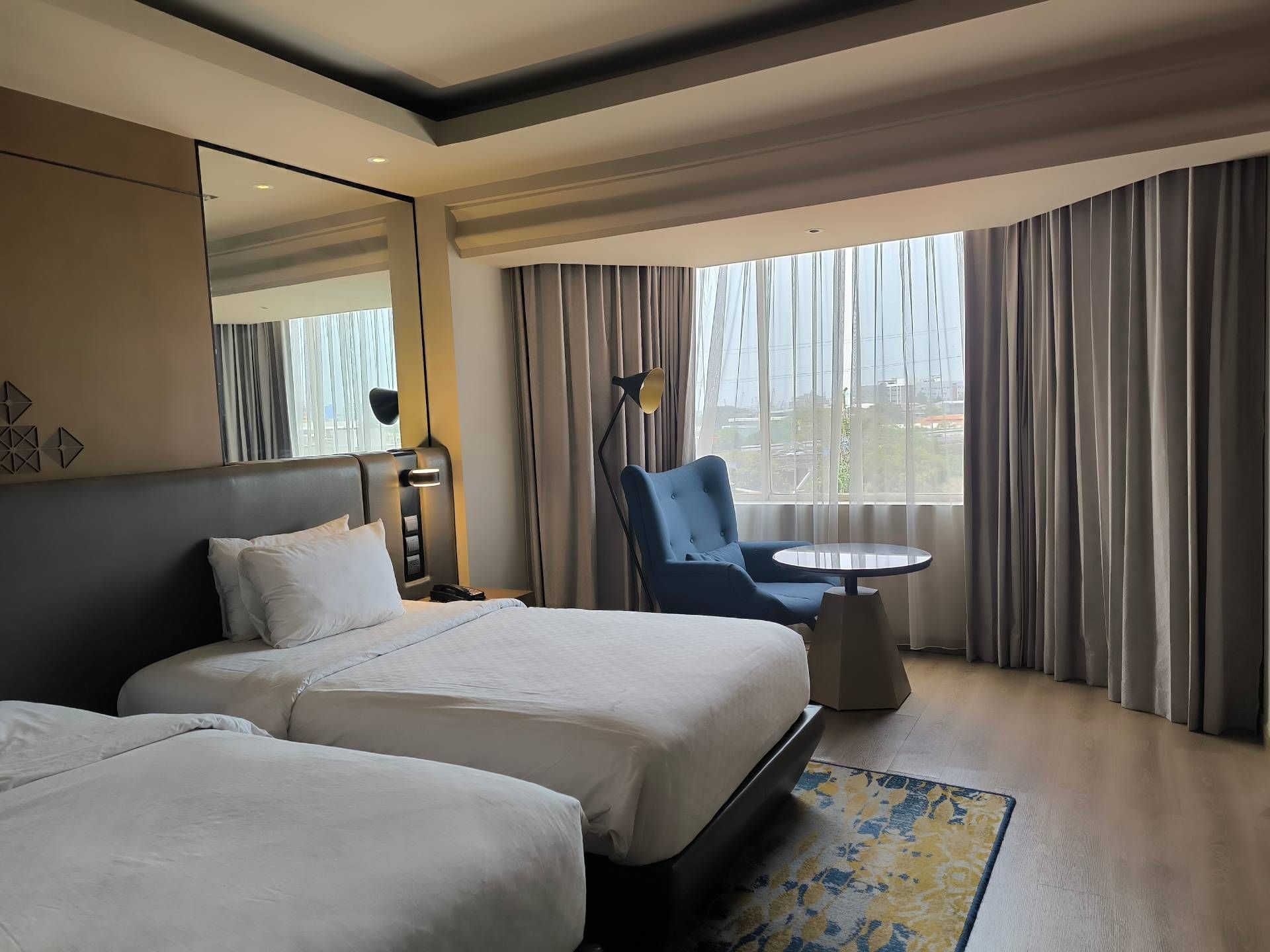 Hotel room with two beds, a chair, and a table near a window with curtains.