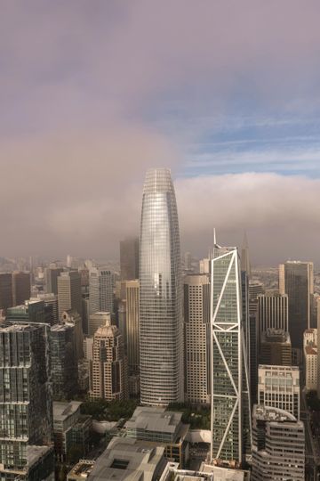 City skyline with a tall silver skyscraper, dense high-rises, and a cloudy sky at dusk