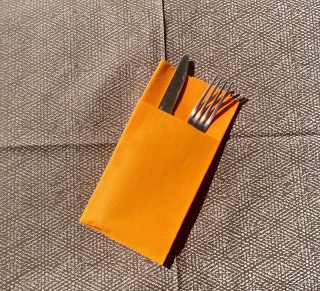 Porte-couverts orange avec une fourchette et un couteau sur une nappe à motifs marron.