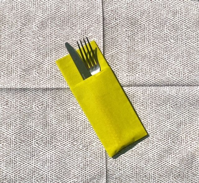 Porte-ustensiles jaune avec couteau et fourchette sur une serviette à motifs gris.