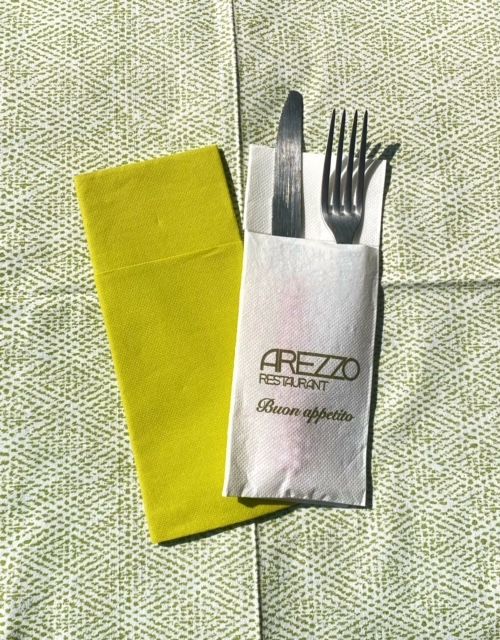 Serviette jaune et porte-couverts blanc du restaurant Arezzo avec couteau et fourchette sur une nappe verte.