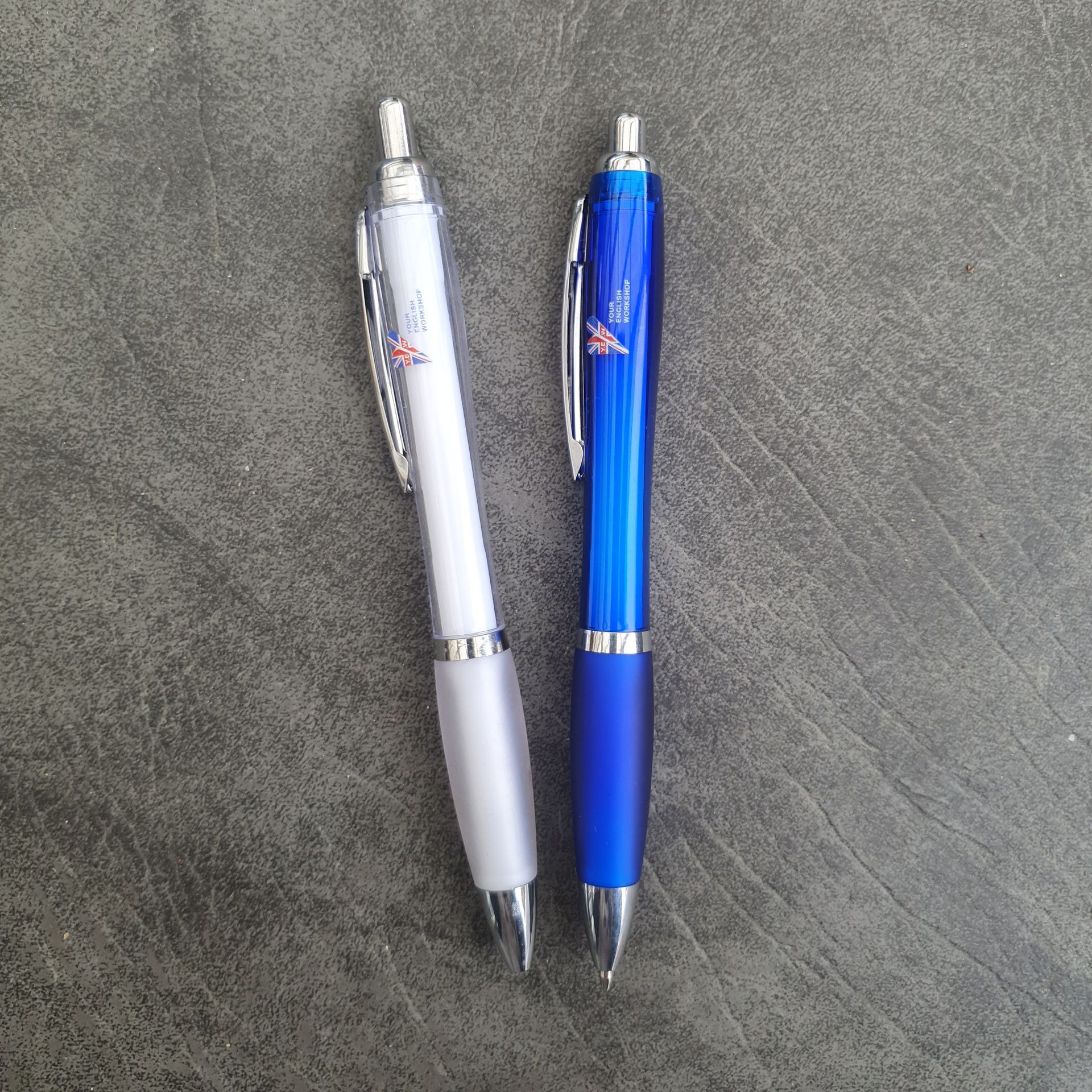 Deux stylos à bille : un blanc, un bleu, côte à côte sur une surface grise.