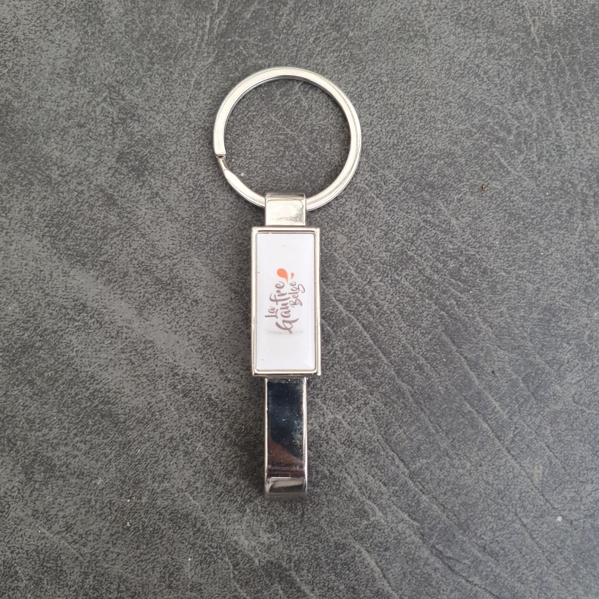 Porte-clés en métal blanc et argent, avec texte.