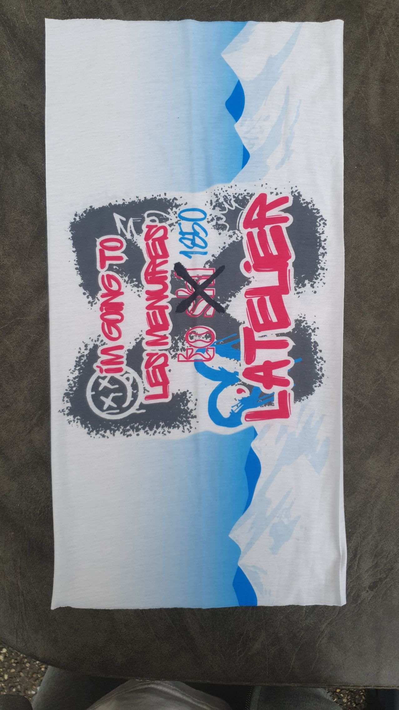 Couvre-visage blanc avec texte de style graffiti : « LATER », « LES ENNUIS » et « IN INTERESTED » sur des montagnes bleues et blanches.