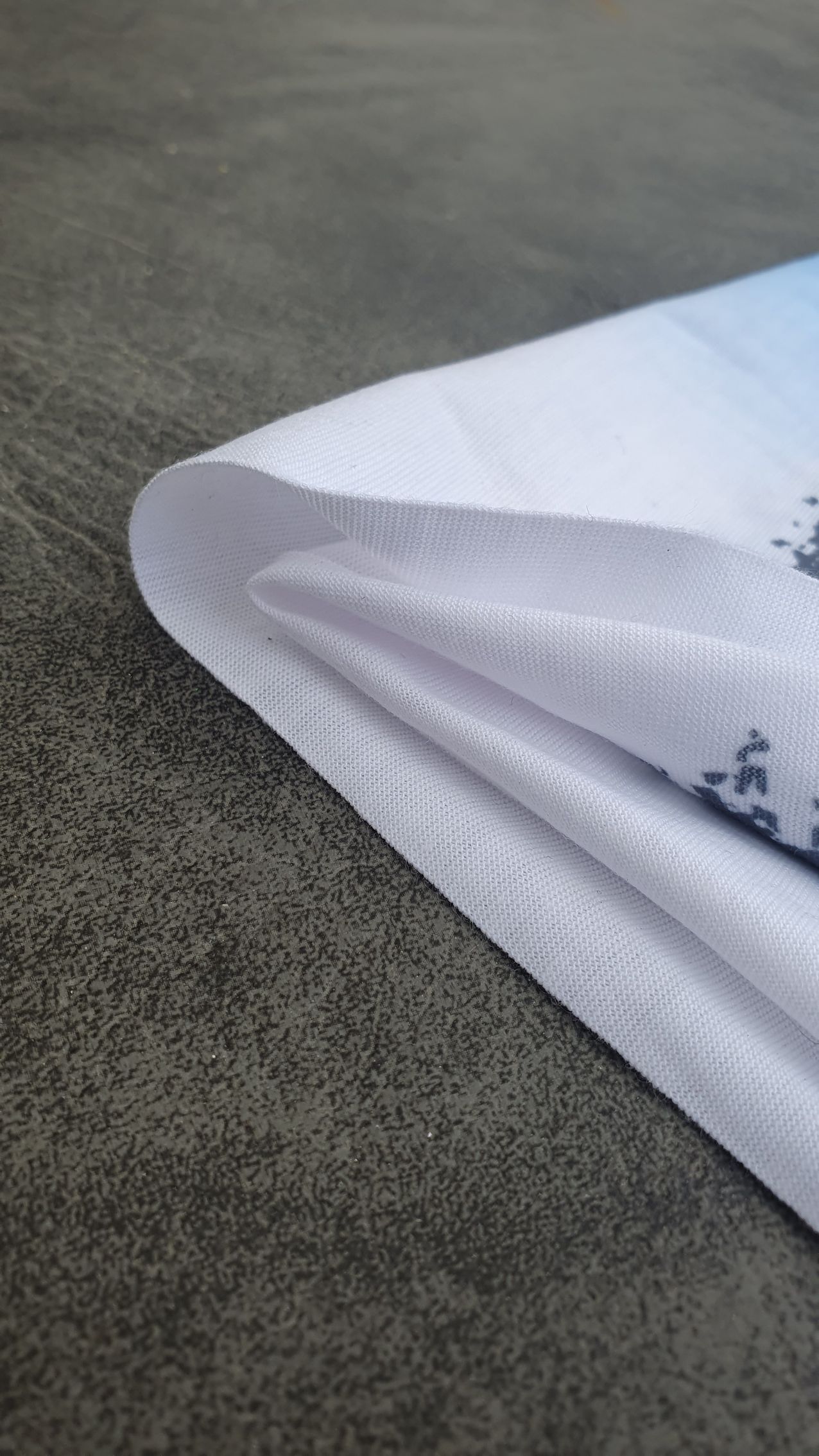 Tissu blanc plié avec un dégradé bleu, texturé sur une surface grise.