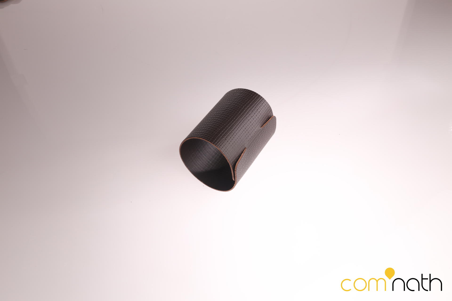 Un objet cylindrique sombre avec une texture visible, peut-être en fibre de carbone, posé sur une surface réfléchissante.