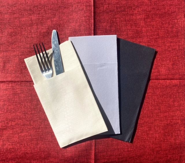 Trois porte-serviettes en papier pliés sur une nappe rouge ; un avec une fourchette et un couteau.