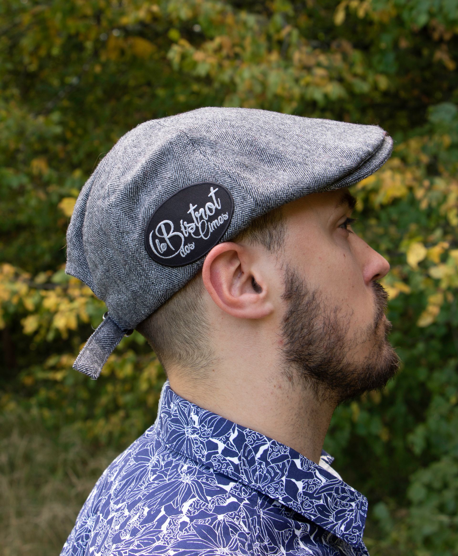Homme portant une casquette plate à motifs gris avec logo, portant une chemise à fleurs bleue, à l'extérieur.