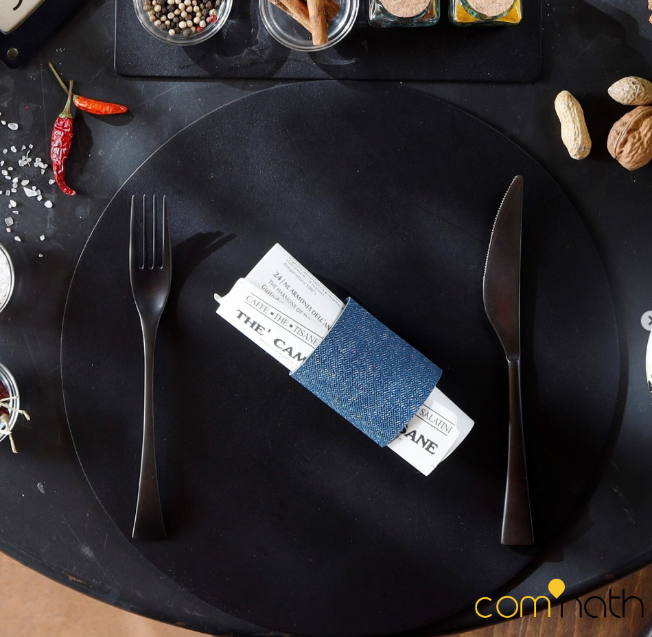 Table noire avec assiette, fourchette, couteau, serviette et condiments.