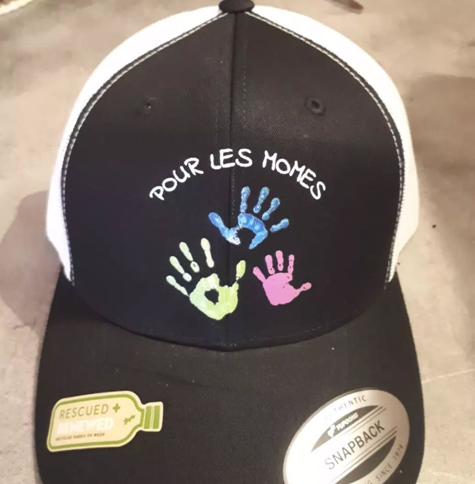 Casquette de baseball noire et blanche avec « POUR LES HOMES » et des empreintes de mains colorées ; un autocollant « RESCUED » est sur le bord.