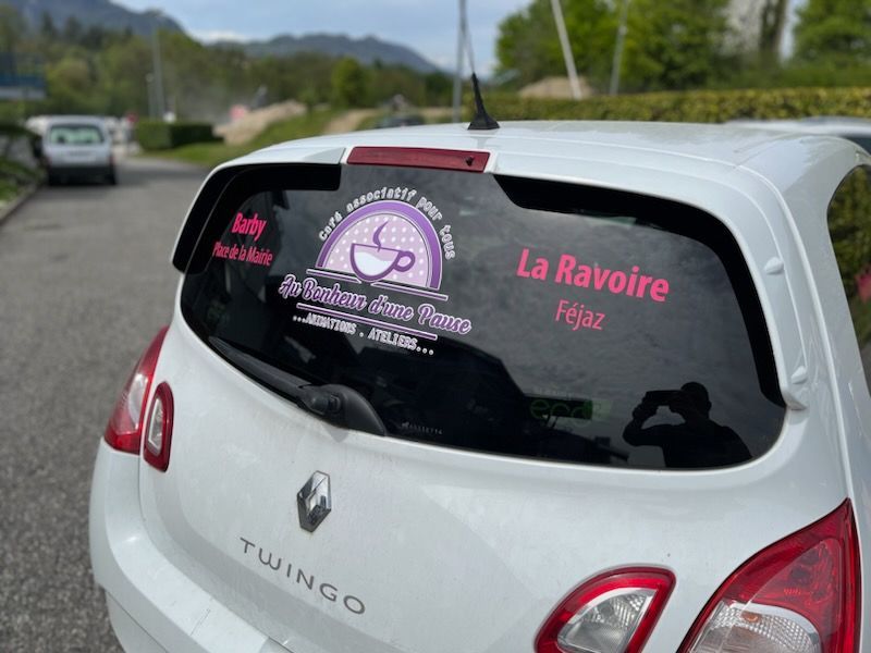 Renault Twingo blanche avec stickers pour lunette arrière pour un café : La Ravoire. Lettrage rose et motif tasse à café.