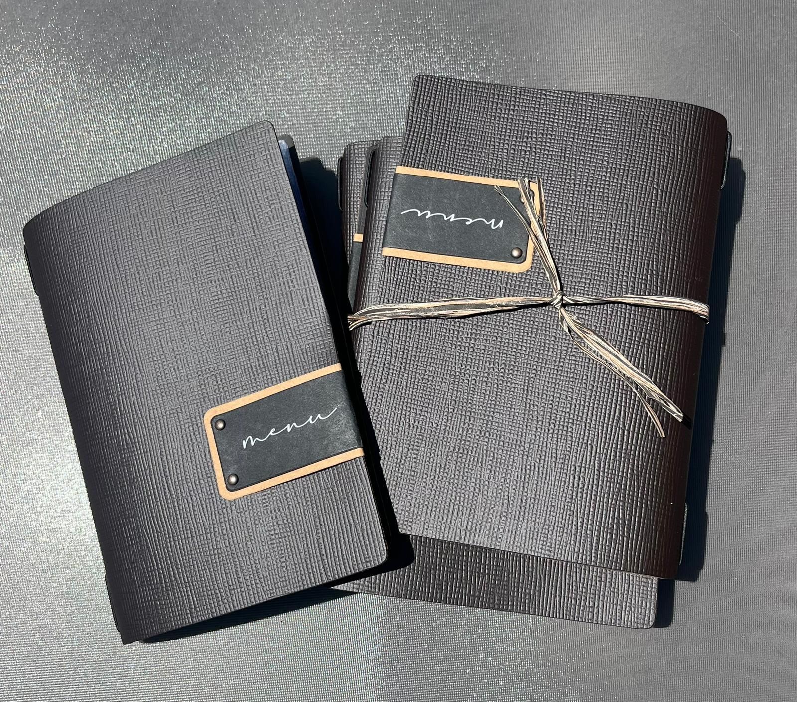 Deux cahiers reliés, l'un gris et l'autre marron foncé, étiquetés avec de petites étiquettes, attachés avec de la ficelle.