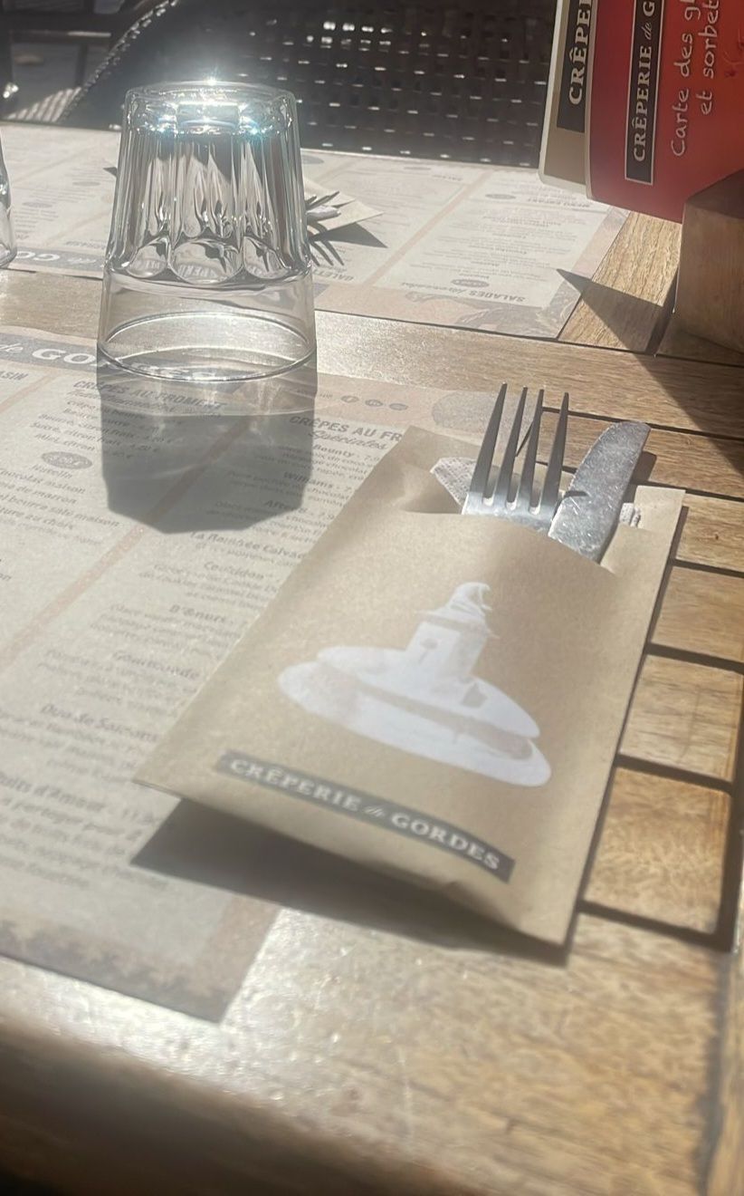 Un verre d'eau, des couverts dans un paquet, sur une table de restaurant.