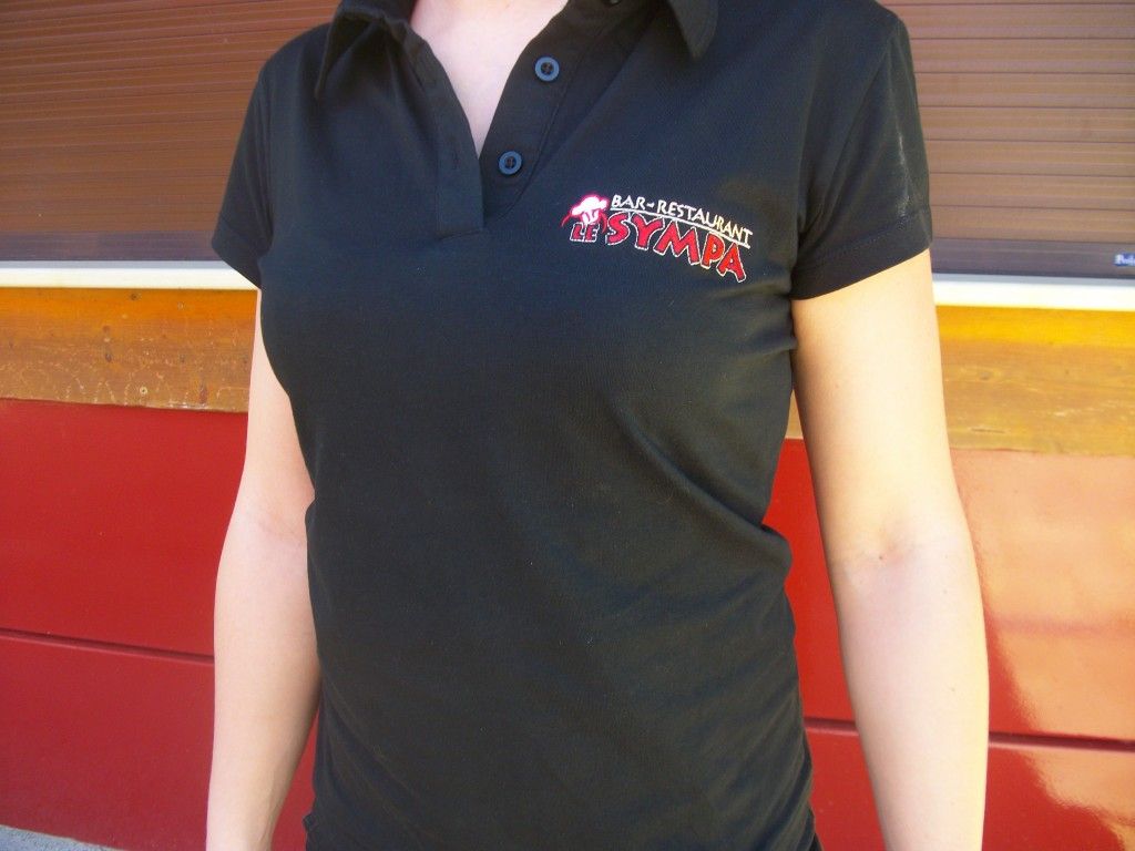 Femme portant un polo noir avec un logo rouge.