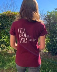 Femme portant un t-shirt marron avec un texte blanc sur lequel on peut lire « Insolite, Plus qu'on le dit ».
