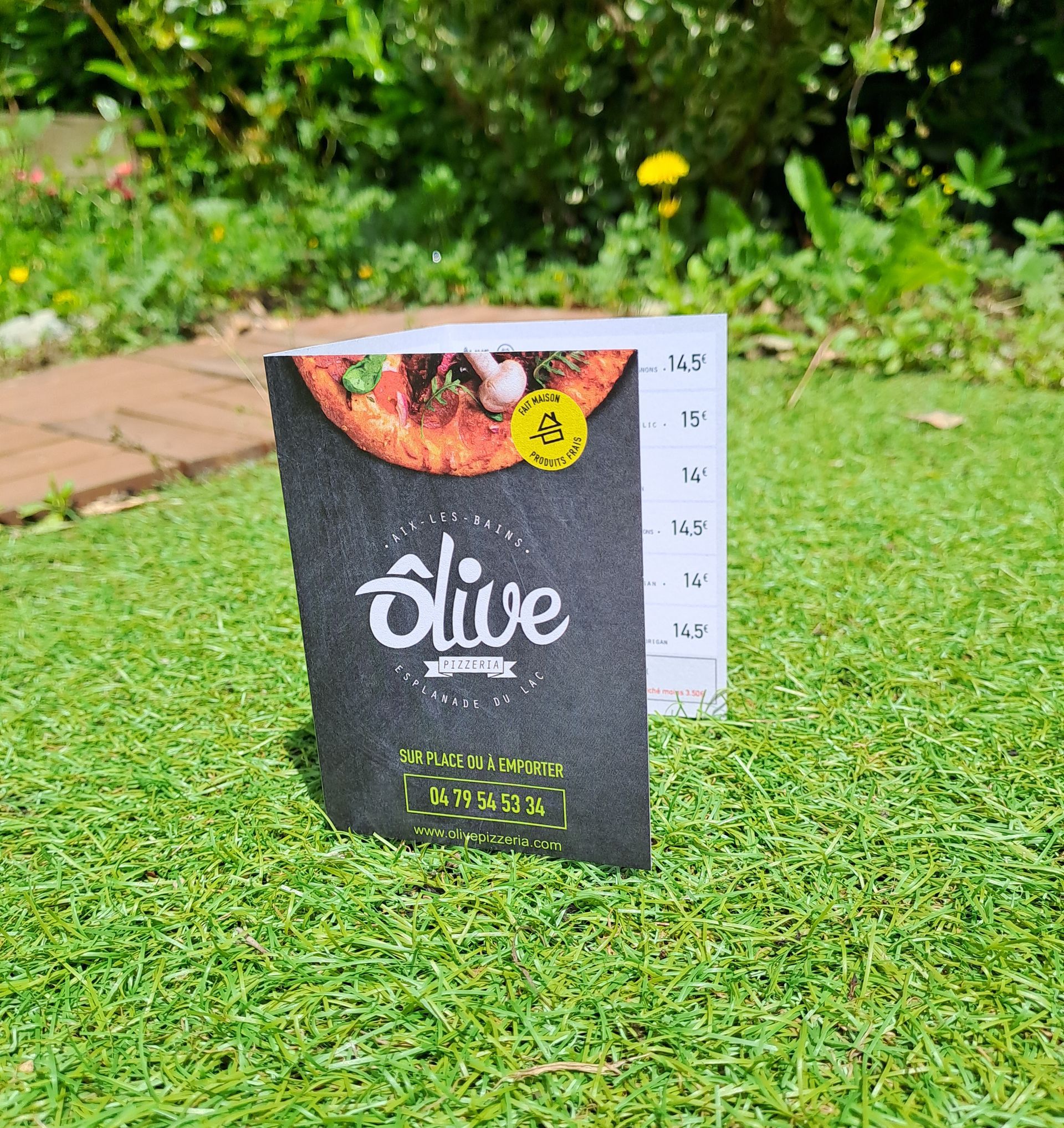 Menu à trois volets sur herbe verte. Au recto, le logo du restaurant et un numéro de téléphone.