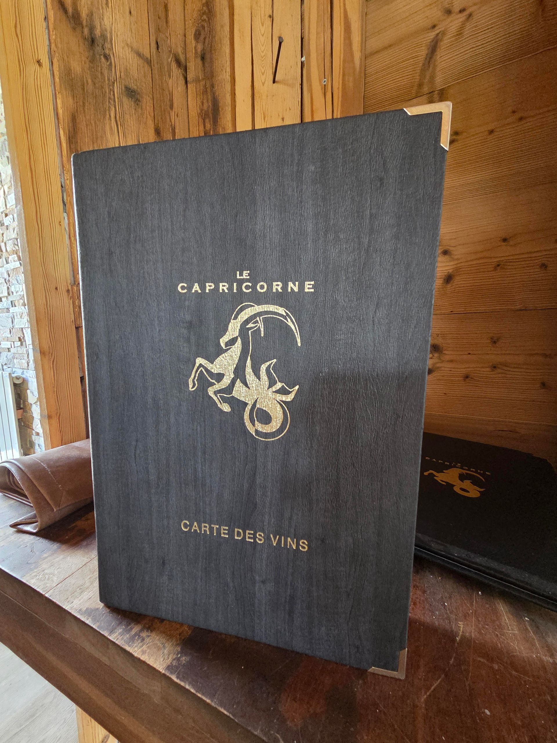 Un menu intitulé « Le Capricorne » avec des lettres dorées et le symbole du Capricorne, sur une surface en bois.
