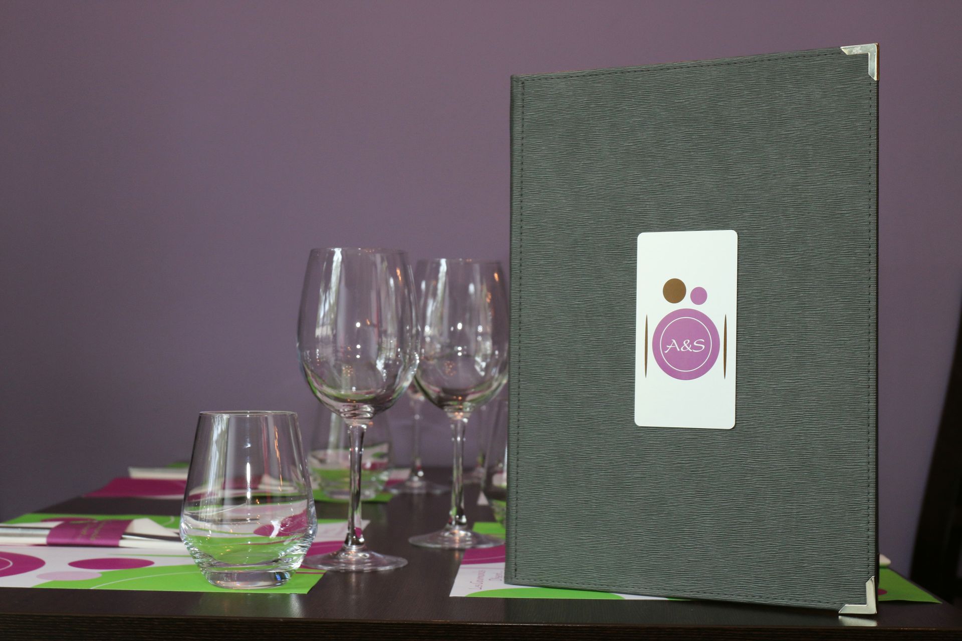 Verres à vin et menu sur une table avec un mur violet en arrière-plan.