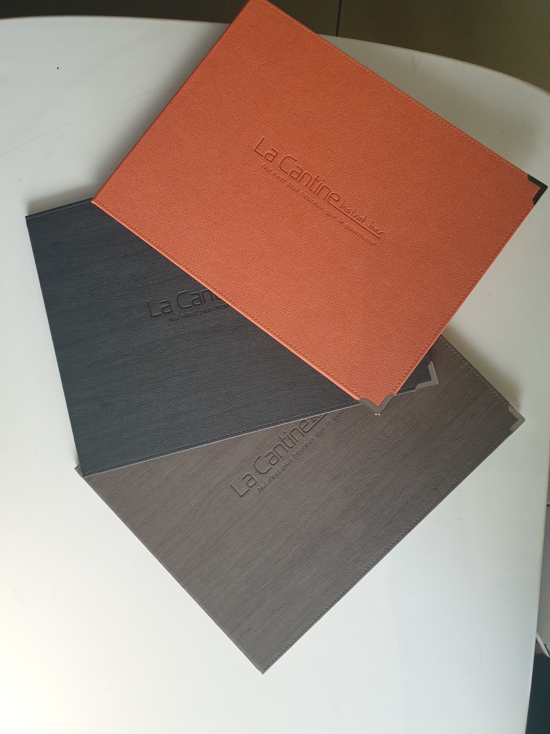 Trois carreaux carrés texturés, orange, noirs et marron, se chevauchant sur une surface blanche.