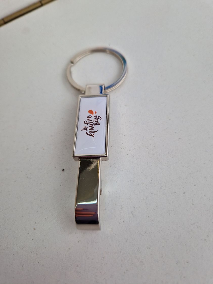 Porte-clés argenté avec une étiquette blanche rectangulaire avec du texte orange et noir et un clip en métal.
