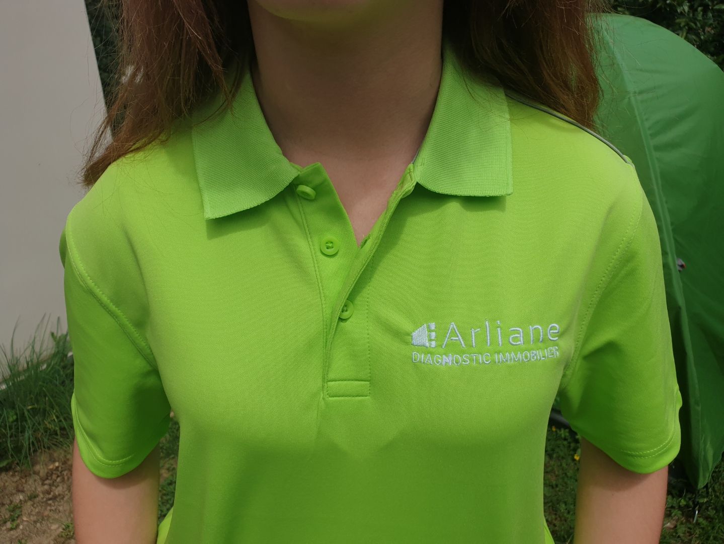 Femme portant un polo vert vif avec un logo indiquant « Arliane » dessus.