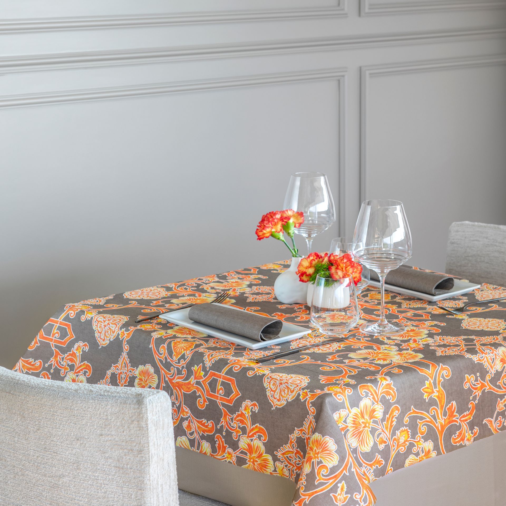 Table dressée pour un repas avec nappe à motifs, fleurs, verres à vin et serviettes.